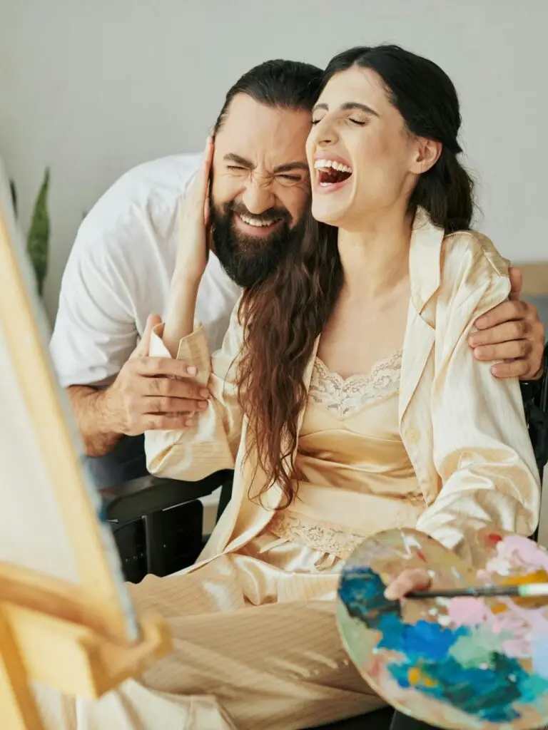 appealing cheerful couple of bearded man and disabled woman painting on easel together at home